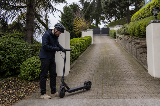 Helmeted adult checking an electric scooter on a gated private sloped driveway in the UK